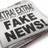 The front page of a newspaper with the headline "Fake News" which illustrates the current phenomena. Front section of newspaper is on top of loosely stacked remainder of newspaper. All visible text is authored by the photographer. Photographed in a studio setting on a white background with a slight wide angle lens.